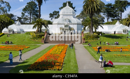 Das Conservatory of Flowers im Golden Gate Park, San Francisco, bietet lebhafte Blumenbeete, Palmen und Besucher, die einen sonnigen Tag genießen. Stockfoto