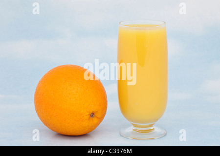 Ein Glas frischen Orangensaft mit einer ganzen orange mit Vitamin C vor blauem Himmel Hintergrund Stockfoto