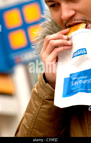 Ein Mann isst seine vor kurzem kaufen Greggs Essen. Stockfoto