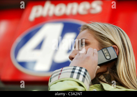 Bild zeigt eine Frau mit ihrem Handy außerhalb eines Handys 4u Store auf der Oxford Street, London. Stockfoto