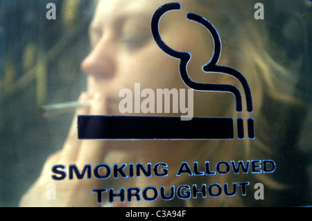 Eine junge Frau mit einer Zigarette Pause auf ein Zeichen "Rauchen erlaubt" Stockfoto