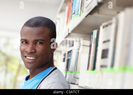 junge afrikanische amerikanische College-Studentin in Bibliothek, Blick in die Kamera in der Nähe von Regal Stockfoto