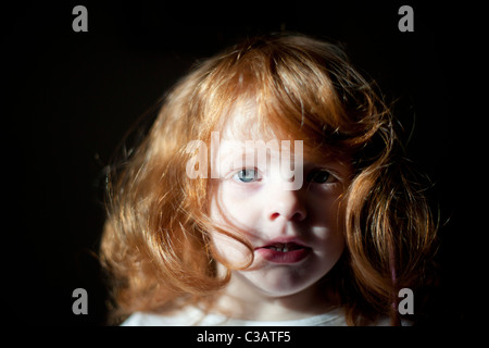 Porträt eines vier Jahre alten Mädchens mit dem roten Haar auf einem schwarzen Hintergrund. Stockfoto