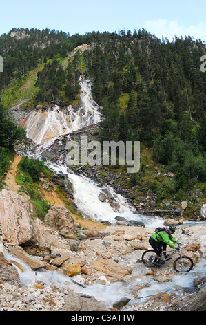 Ein Mountainbiker fährt vorbei an einem Bach unter einem Wasserfall im Bereich Les Avals des Skigebietes Courchevel in Frankreich Stockfoto