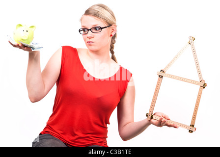 junge Frau mit klappbarem Regel als Haus-Symbol und Sparschwein vor weißem Hintergrund Stockfoto