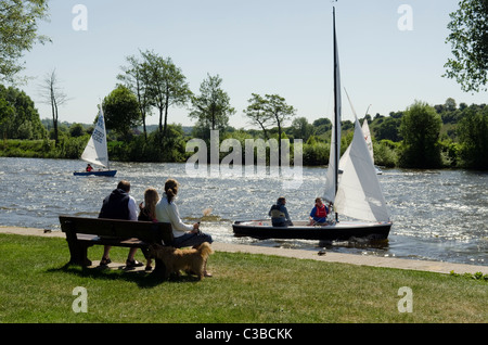 Familie sitzt auf einer öffentlichen Bank auf dem Fluss Themse Bourne End Segeljollen beobachten. Stockfoto