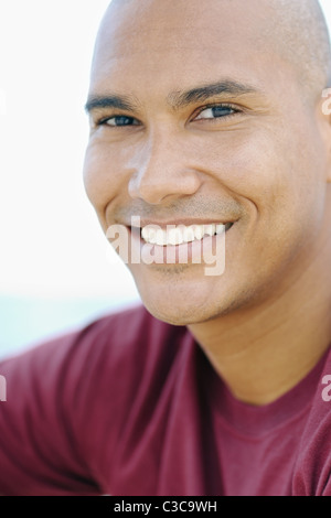 Porträt des jungen hispanischen Kerl mit rasierten Kopf, Blick in die Kamera in der Nähe des Meeres. Vertikale Form, Kopf und Schultern Stockfoto