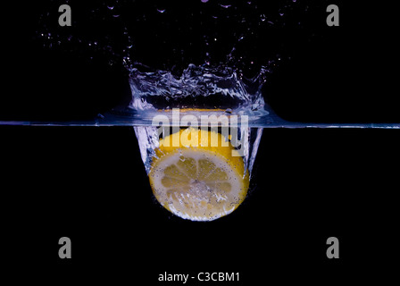 Zitrone, planschen im Reinwasser auf schwarzem Hintergrund isoliert Stockfoto