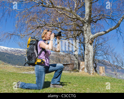 junge hübsche Frau kniet in den Bergen um das perfekte Bild, gekleidet in Wanderausrüstung mit Rucksack zu erhalten Stockfoto