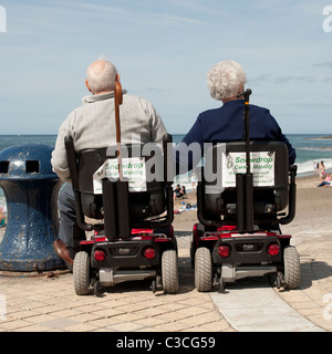 Rückansicht des eine ältere Behinderte paar Mann und Frau am Meer sitzen in powered Scooter, Aberystwyth, Wales Stockfoto