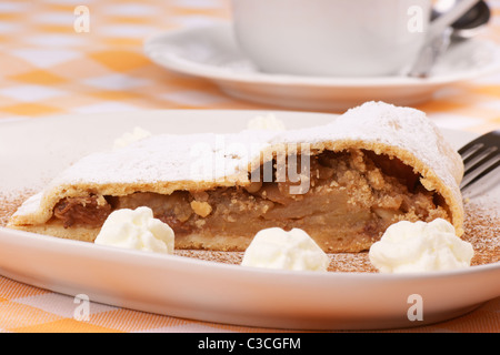 Apfelstrudel (Apfelstrudel) mit einer Teetasse im Hintergrund auf einem weißen Teller serviert. Stockfoto