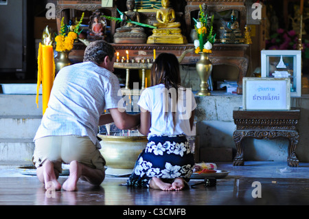 Ein Mann und eine Frau beten an einem buddhistischen Altar, kniend und Weihrauch vor Kerzen, Bilder und Statuen. Stockfoto