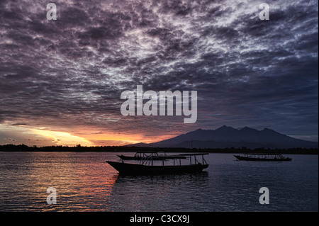 Tagesanbruch über die Boote in den ruhigen tropischen Gewässern im Schatten des Mount Rinjani Vulkan, Lombok, Indonesien Stockfoto