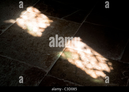 Sonnenlicht durch ein Bleiglas Fenster strömt und wirft Schatten auf einem alten Stein Flagge Stock. Stockfoto