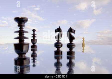 Chessmans auf Spiegel und bewölktem Himmelshintergrund Unschärfe Stockfoto