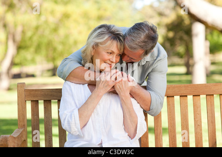 Älterer Mann umarmt seine Frau, die auf der Bank Stockfoto