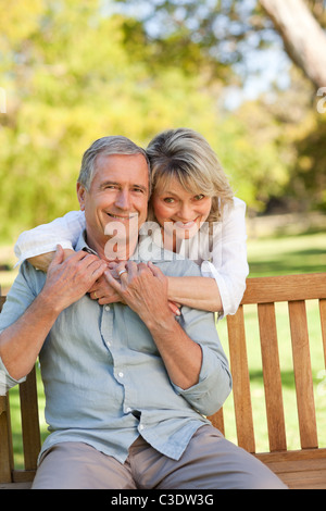 Ältere Frau umarmt ihrem Mann auf der Bank Stockfoto