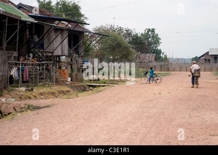 Menschen sind Fahrräder auf einer unbefestigten Straße in einem typischen Viertel in ländlichen Kratie, Kambodscha Reiten. Stockfoto