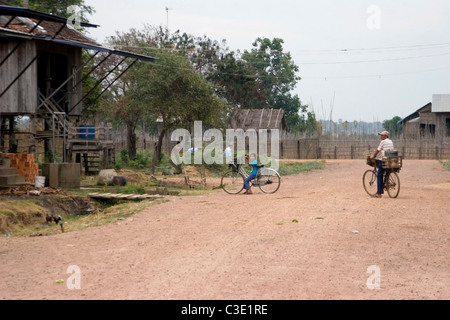 Menschen sind Fahrräder auf einer unbefestigten Straße in einem typischen Viertel in ländlichen Kratie, Kambodscha Reiten. Stockfoto