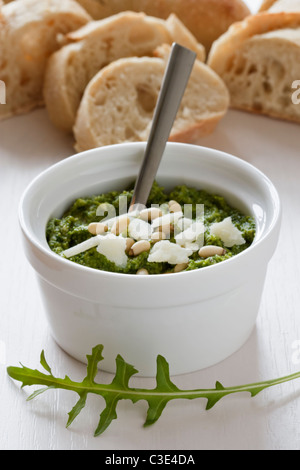 Eine kleine weiße Schale mit vorbereiteten Rucola-Pesto mit Pinienkernen auf einem hölzernen Hintergrund. Stockfoto