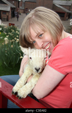 Nachlass von Tatton Park, England. Lady Besucher Kuscheln ein Neugeborenes Lamm an Tatton Park Home Farm. Stockfoto