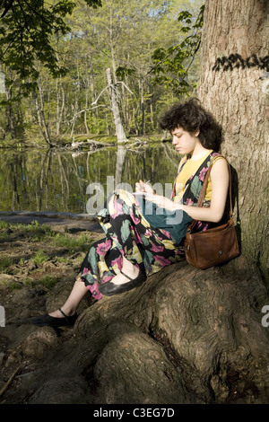 Junge Frau sitzt an einem Baum hat einige schreiben im Prospect Park, Brooklyn, NY. Stockfoto