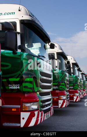 Reihe geparkter Eddie Stobart-Lastwagen, Zugmaschinen, Anhänger und Container bei LKW-Haltestelle. Reihe von Lackierung AEC Scania R440 Transportfahrzeuge. Stockfoto