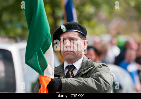 Mann in Uniform paramilitärischer Stil hält eine irische Trikolore als Teil einer Farbe-Partei an der Spitze einer republikanischen Parade. Stockfoto