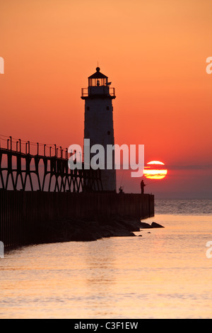 Ein einsamer Fischer ist am Fuße des Leuchtturms an einem Sommerabend an der 5th Avenue Beach in Manistee, Michigan Silhouette. Stockfoto