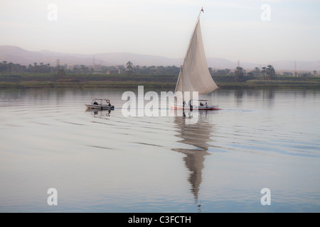 Feluke abgeschleppt mit dem Motorboot auf dem Nil bei Sonnenuntergang, Luxor, Ägypten, Nordafrika Stockfoto