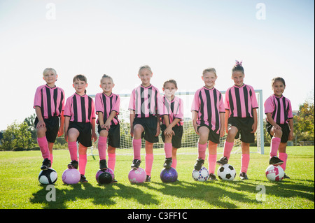 Mädchen-Fußball-Spieler stehen mit Füßen auf Fußbälle Stockfoto