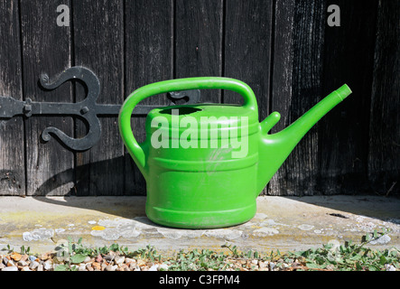 Eine grüne Gießkanne stehen an der Schwelle einer alten Tür. Stockfoto