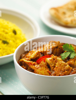 Hühnchen-Curry in Schüssel mit Pilau Reis und Naan Brot. Curry ist mit Koriander-Blättern garniert. In weißem Geschirr vorgestellt. Stockfoto