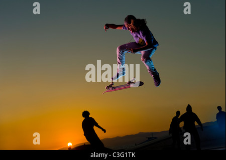 Kaukasische Skateboarder Stunt in der Luft zu tun, bei Sonnenuntergang Stockfoto