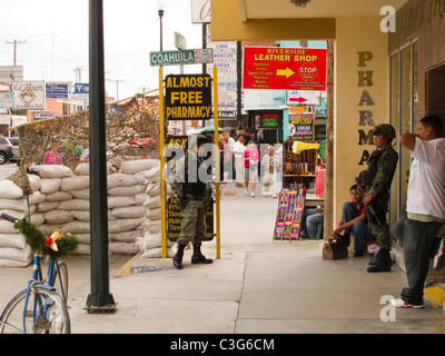 Bewaffneten mexikanische Soldaten stehen in der Nähe ihrer befestigten Post, während Touristen und Straßenhändler ihre Geschäfte in Nuevo Progreso zu machen. Stockfoto