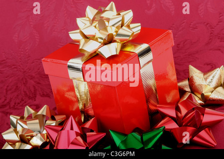 Eine rote Weihnachten Geschenk-Box mit goldenen Bändern umgeben von bunten Bögen. Stockfoto