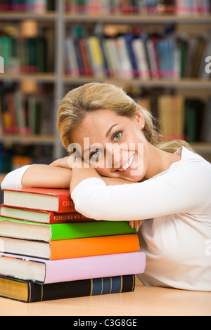 Foto von lächelnden Lehrer setzen ihren Kopf über Stapel von Büchern und Blick in die Kamera Stockfoto