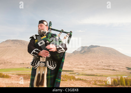 Eine schottische Piper in traditioneller Tracht als Straßenmusikant auf Rannoch Moor in Argyl, Scotland, UK. Stockfoto