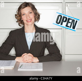 Lächelnde Geschäftsfrau sitzen am Schreibtisch neben Schild "geöffnet" Stockfoto