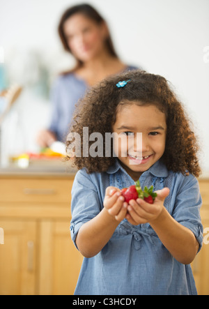 Lächelndes Mädchen unscharf gestellt (6-7) Betrieb Erdbeeren mit Frau im Hintergrund Stockfoto