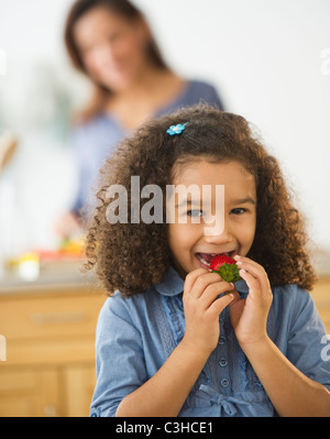 Lächelndes Mädchen (6-7) essende Erdbeeren mit defokussierten Frau im Hintergrund Stockfoto