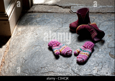 Young Girls bunt gestreiften Fäustlinge und rosa Stiefel auf Schieferboden in einem Hauseingang Stockfoto