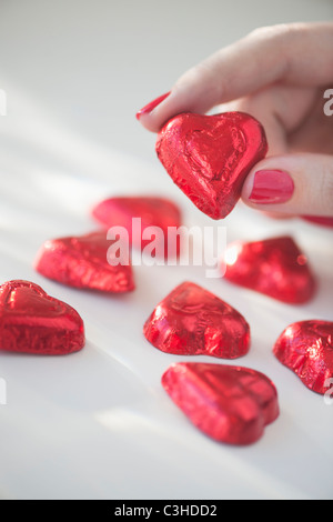 Nahaufnahme von Frau Finger mit rotem Nagellack hält in roter Verpackung Schokolade in Form von Herzen Stockfoto