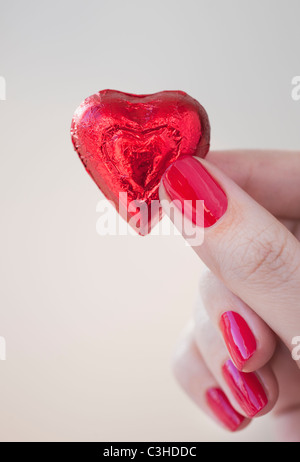 Nahaufnahme von Frau Finger mit rotem Nagellack hält in roter Verpackung Schokolade in Form von Herzen Stockfoto