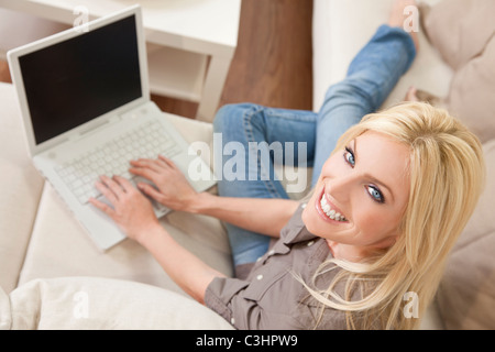 Obenliegende Foto von schönen jungen Frau zu Hause sitzen auf Sofa oder Couch mit ihrem Laptop-Computer und lächelnd Stockfoto