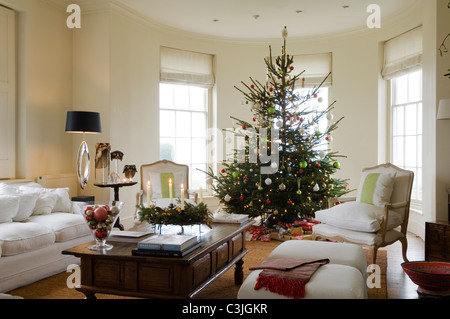 Geschmückter Weihnachtsbaum mit Kugeln im regency Wohnzimmer mit Sesseln und Kerzen Stockfoto