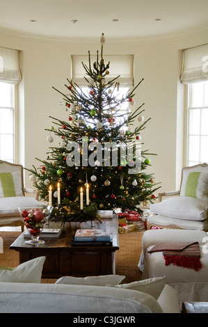 Geschmückter Weihnachtsbaum mit Kugeln im regency Wohnzimmer mit Sesseln und Kerzen Stockfoto