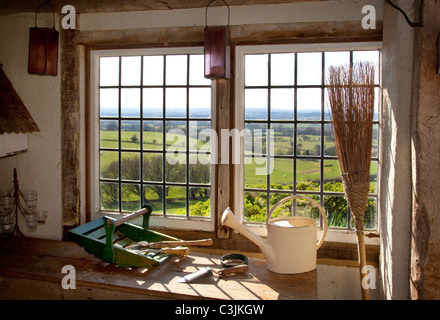 Potting Holzschuppen mit Blick durch Metall gerahmt Fenster, Gartengeräte, Besen, Gießkanne und Holz Trug Korb Holz obenauf Stockfoto