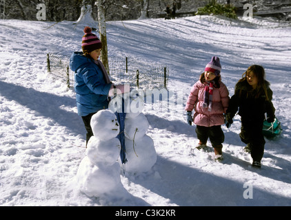USA, New York City, Central Park. Kinder spielen im Schnee und bauen einen Schneemann. Gruppe von Menschen im Park. Nach der Schule. Stockfoto