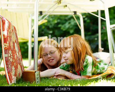 Zwei Mädchen liegen unter Gartentisch und Radio hören Stockfoto